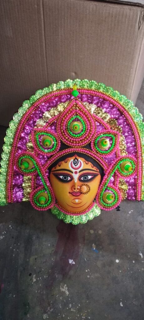 Highlight: Handcrafted traditional Purulia Chhau mask depicting Goddess face in vibrant pink, green, and golden hues. A symbol of folk heritage, this 15x14X6 inch piece by artisan Sanju Shil brings spiritual artistry to life. Perfect for wall decor or cultural collections.